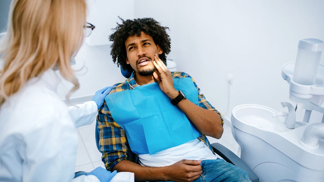 man in dental chair holding hand to jaw